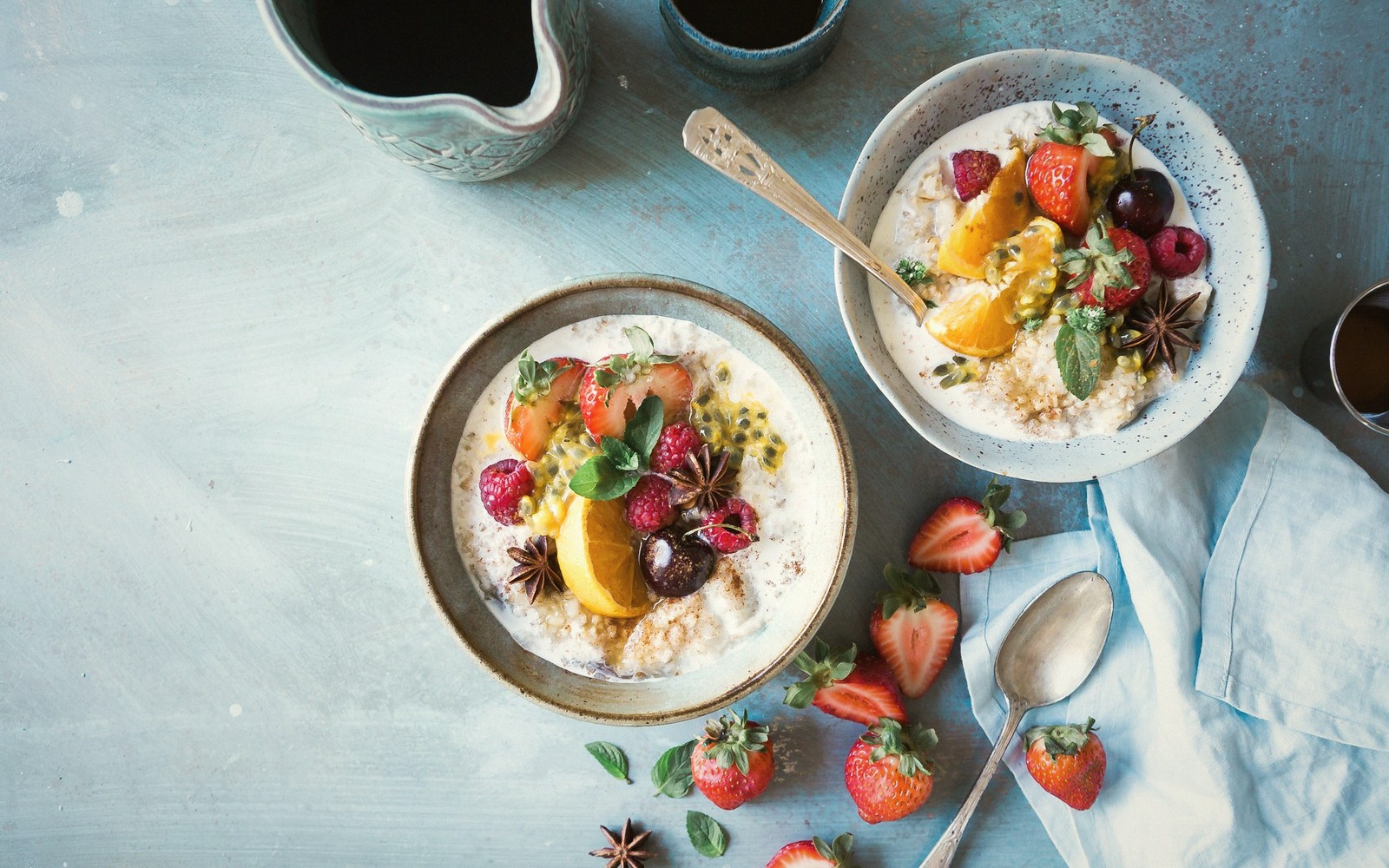 Two bowls of creamy porridge topped with strawberries, oranges, cherries and star anise